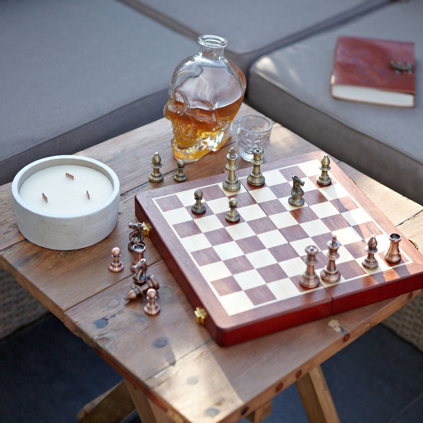 Tablero de ajedrez de madera con piezas de metal, candelero blanco y decoración de cráneo, estilo contemporáneo.