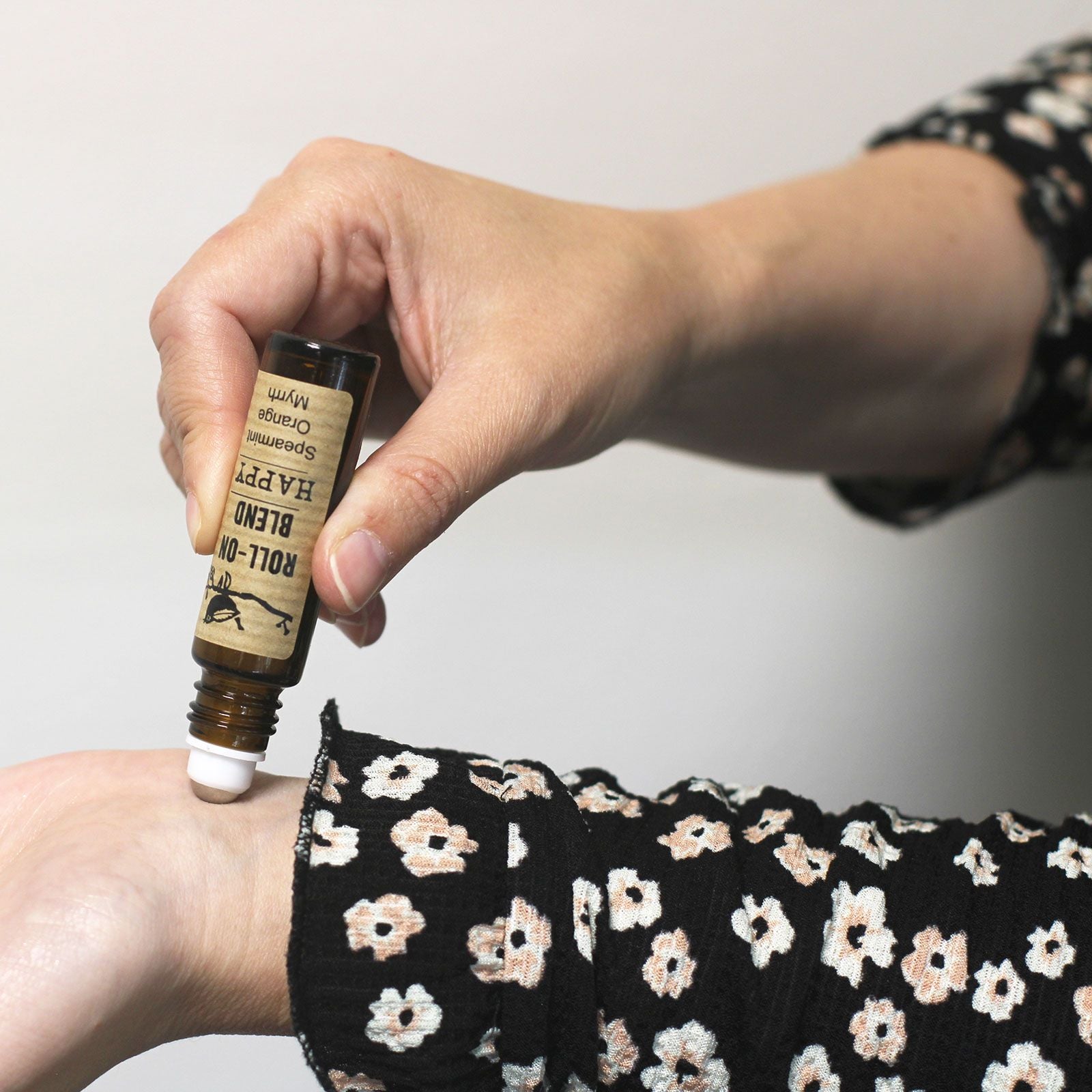 Aceite esencial en frasco ámbar, aplicando mezcla de hierbas en muñeca, camisa negra con flores blancas.