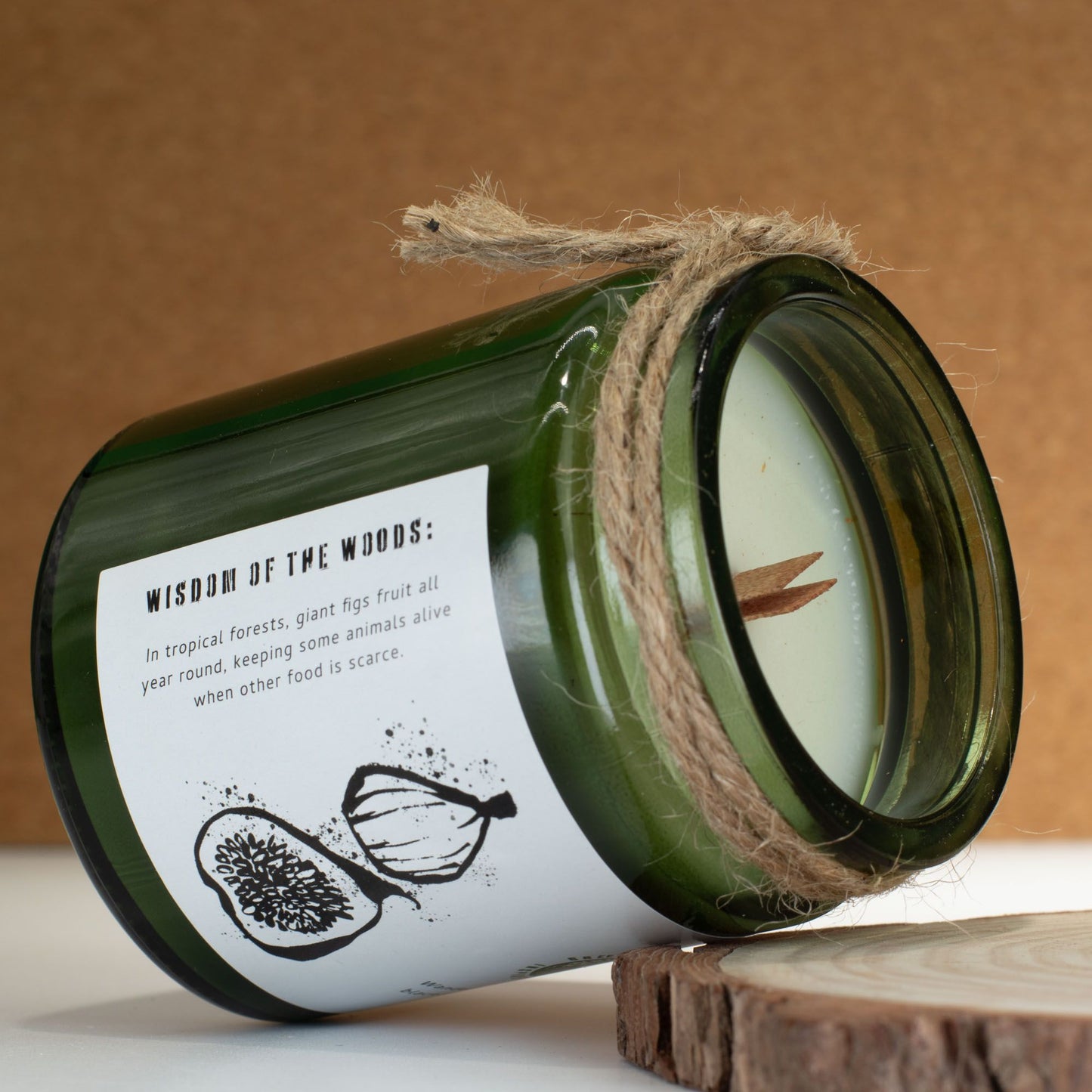 Vela verde de vidrio con etiqueta blanca, aroma a higo y cuerda natural, estilo rústico y ecológico.