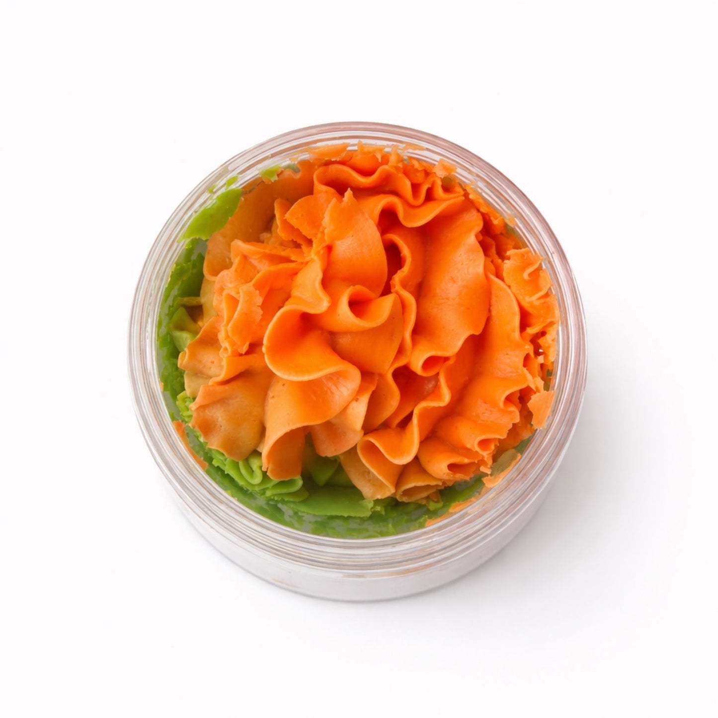 Crema de mantequilla en tonos naranja y verde, con un diseño rizado y elegante en un envase transparente.