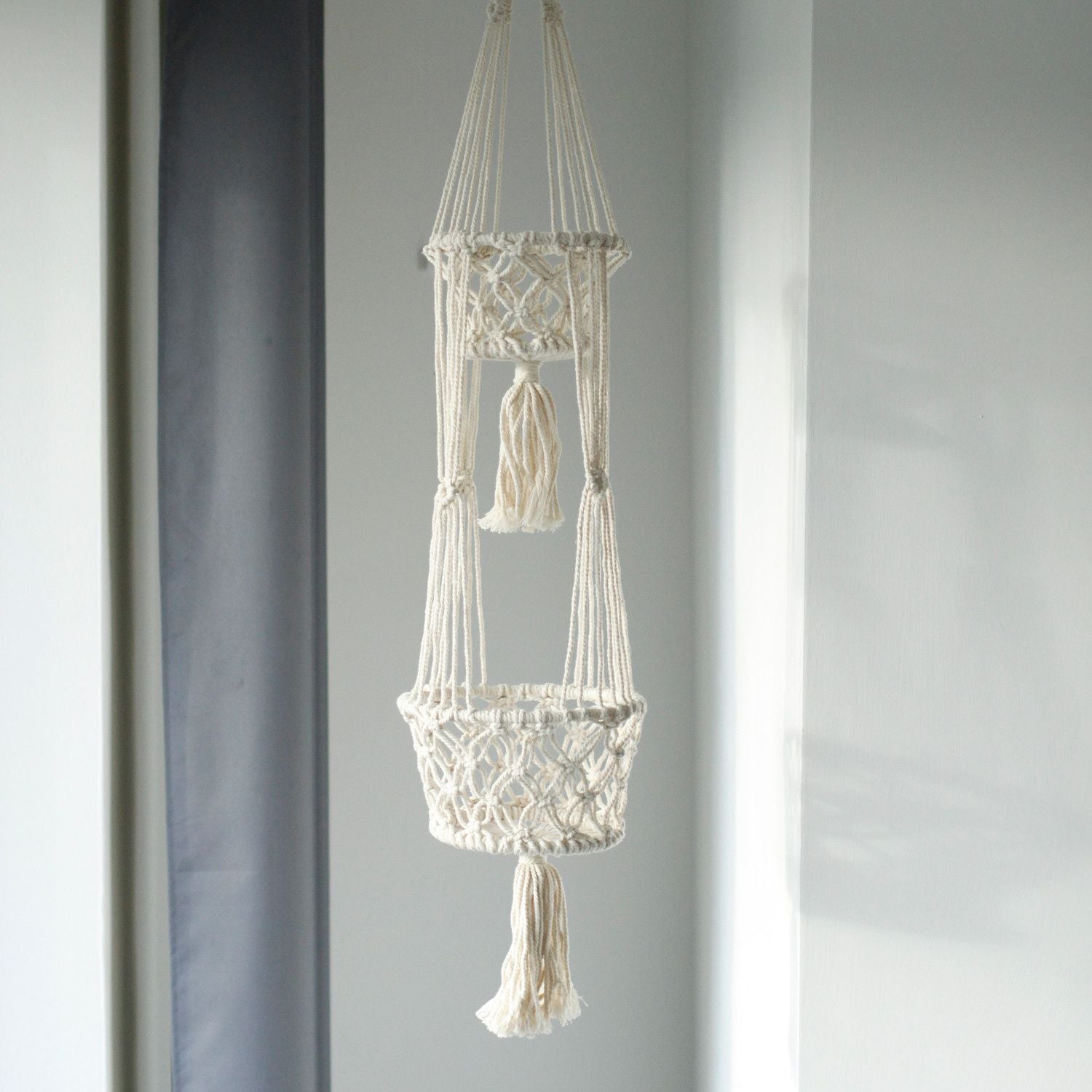 Macramé colgante en color crema con dos cestas decorativas y flecos, ideal para plantas y decoración boho.