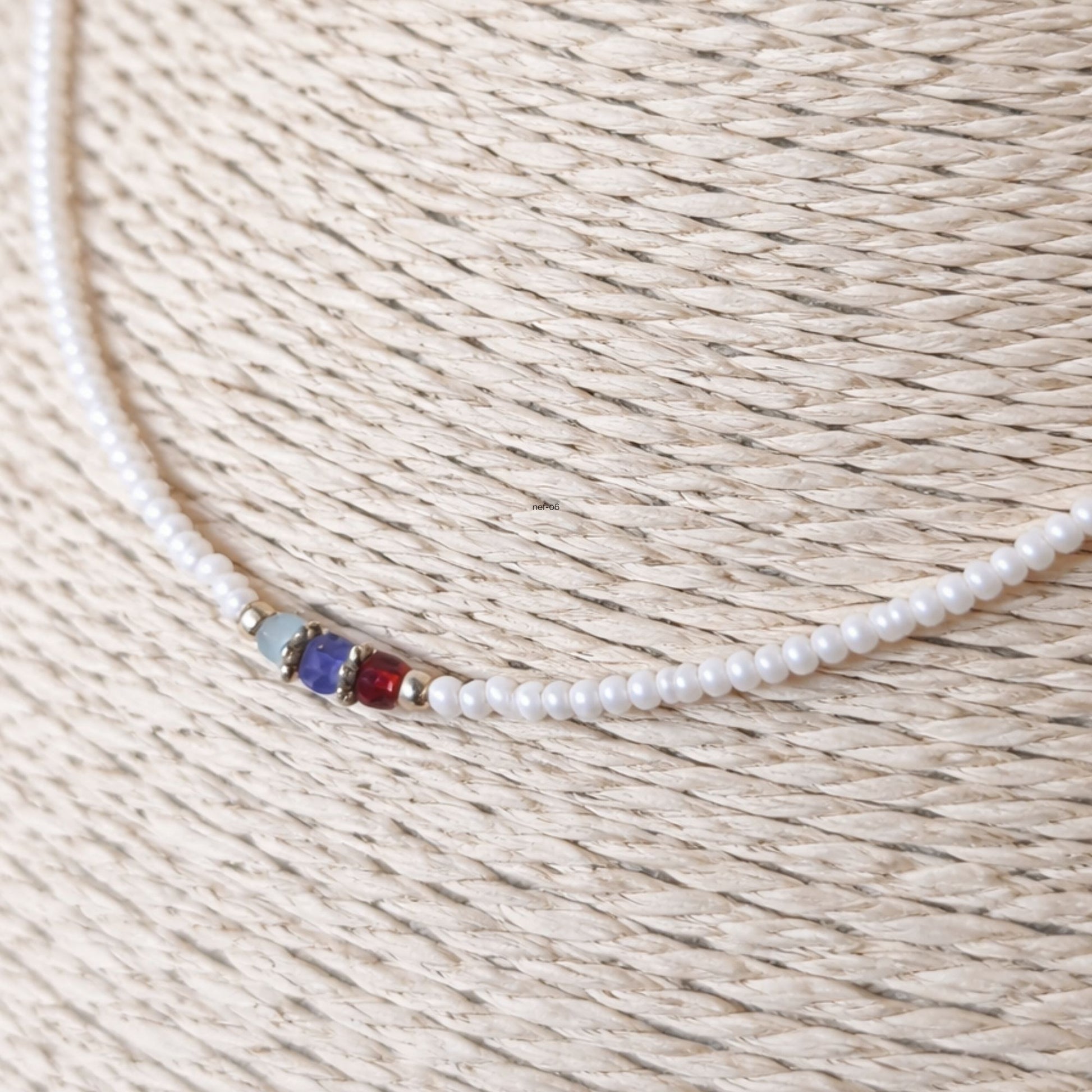 Collar de perlas blancas con detalles en azul y rojo, estilo elegante y moderno, ideal para ocasiones especiales.