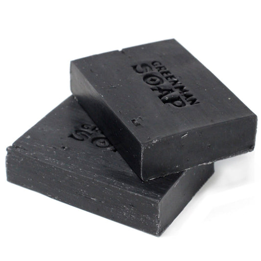 Dos pastillas de jabón rectangulares de color negro intenso, apiladas, con letras grabadas en su superficie.