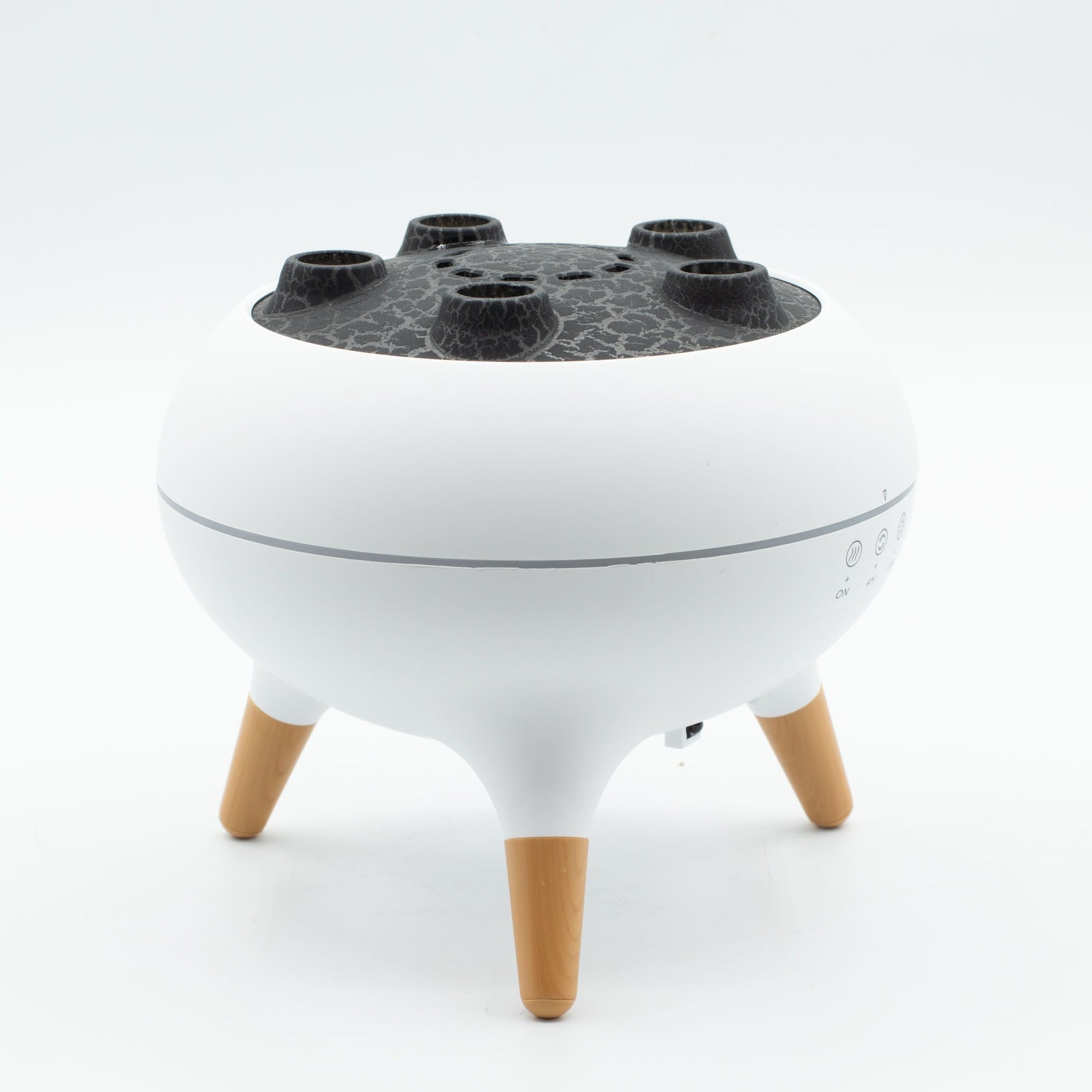 Difusor blanco con tapa negra texturizada, cinco boquillas de vapor y tres patas de madera, diseño moderno.