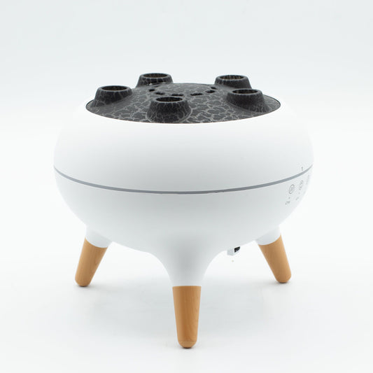 Difusor blanco con tapa negra texturizada, cinco boquillas de vapor y tres patas de madera, diseño moderno.
