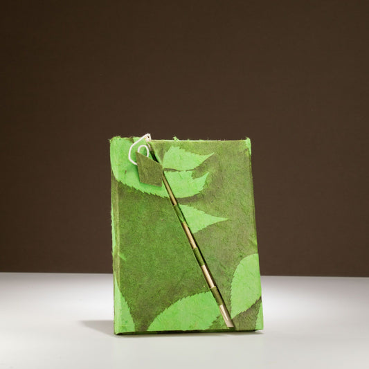 Cuaderno verde de papel reciclado con diseño de hojas, incluye un bolígrafo elegante y ecológico.