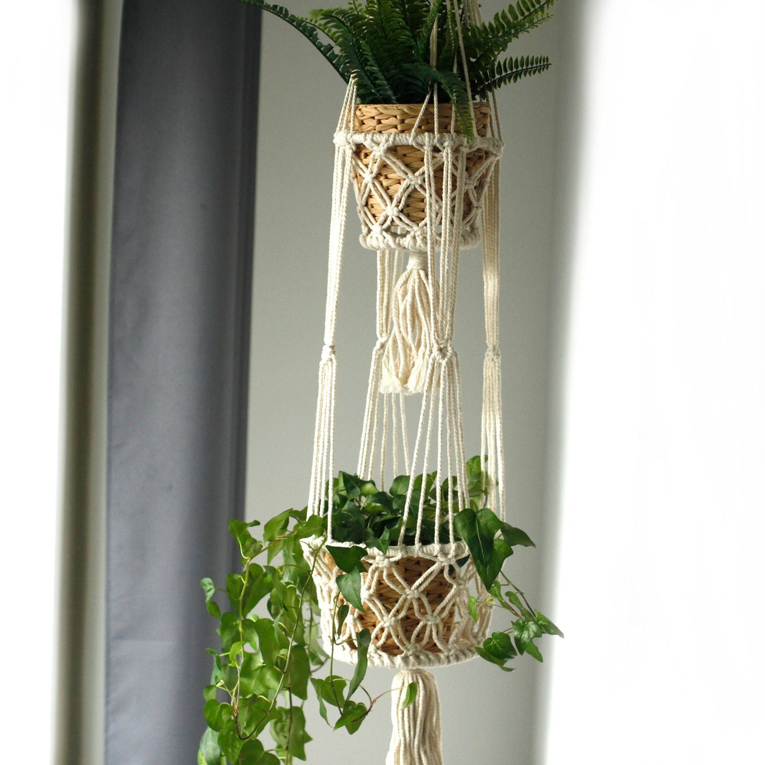 Macramé colgante de algodón color crema con macetas de mimbre y plantas verdes, ideal para decoración bohemia.
