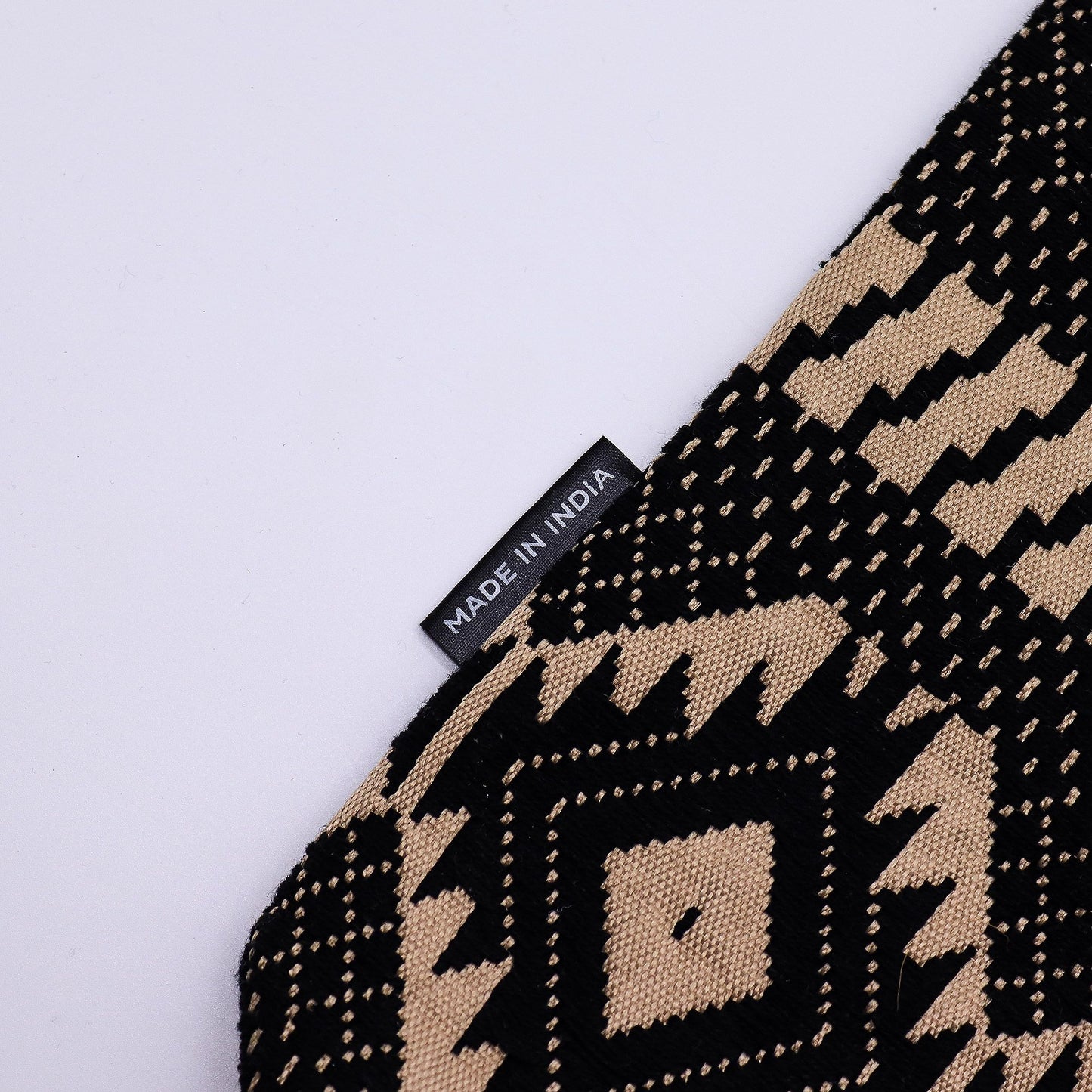 Alfombrilla decorativa de algodón en tonos negro y beige con diseño geométrico, hecha en India.