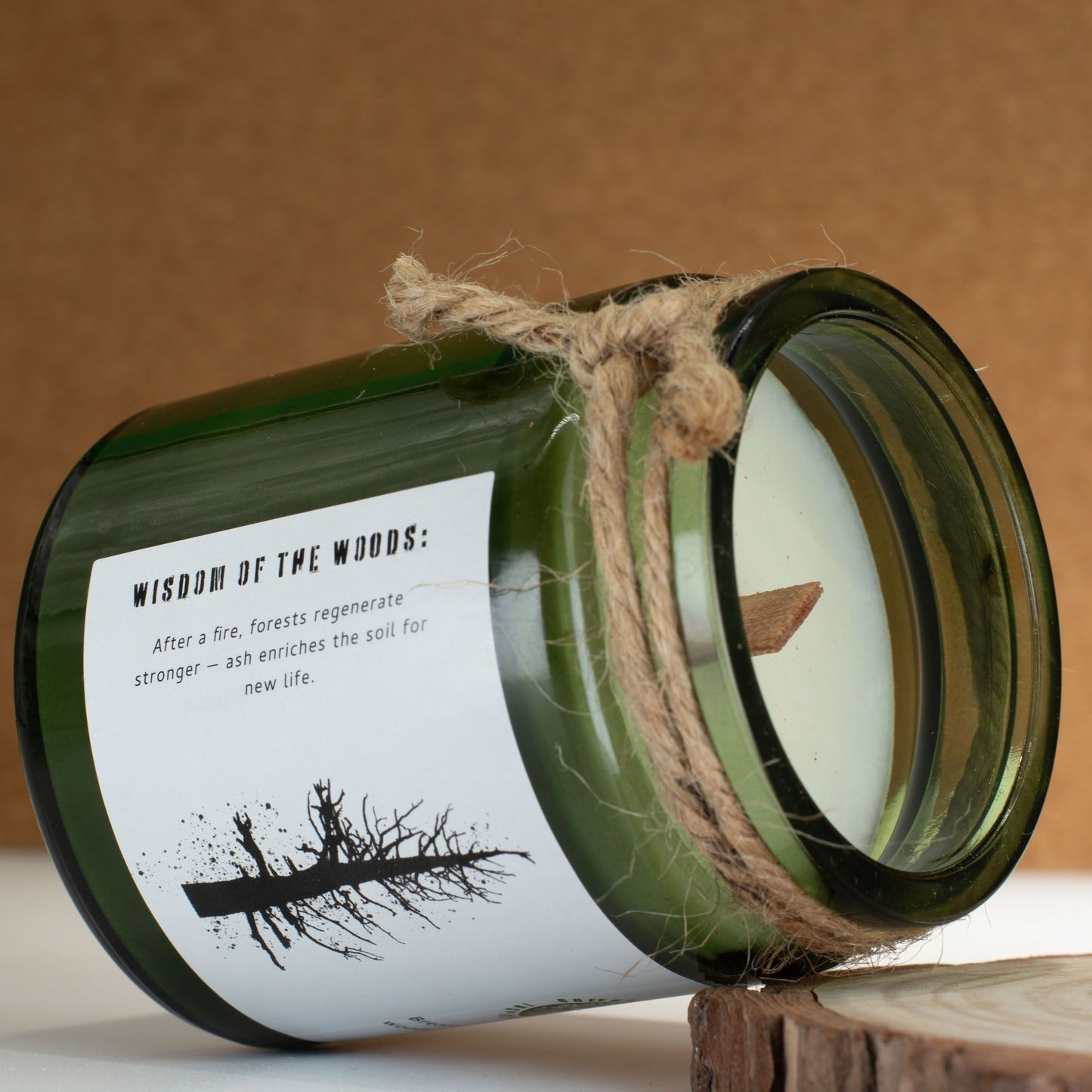 Vela verde en frasco de vidrio con etiqueta "Wisdom of the Woods" y cuerda y tapa de madera. Aromas terrosos.