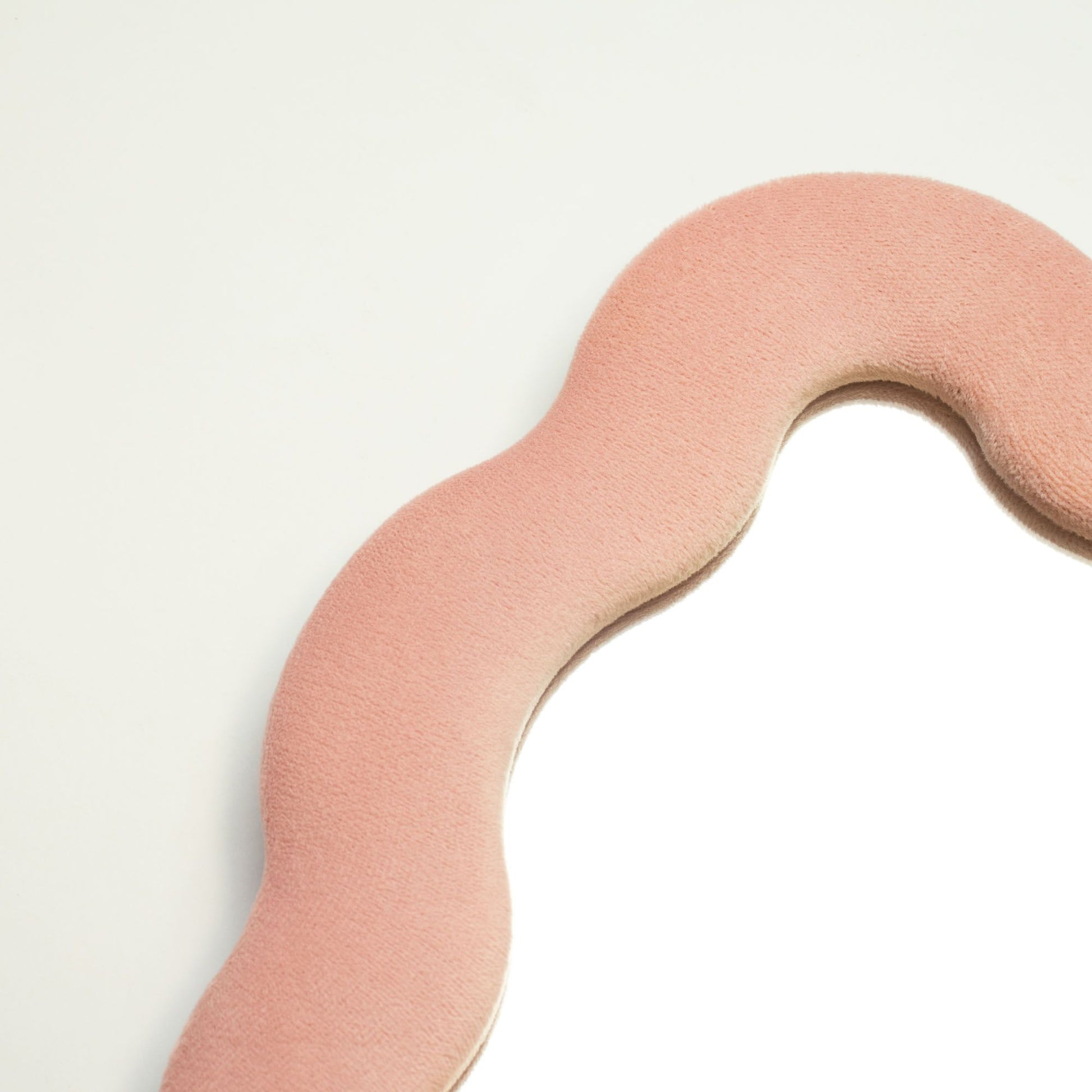 Espejo de forma ondulada con borde de terciopelo rosa y fondo blanco, ideal para decoración moderna.