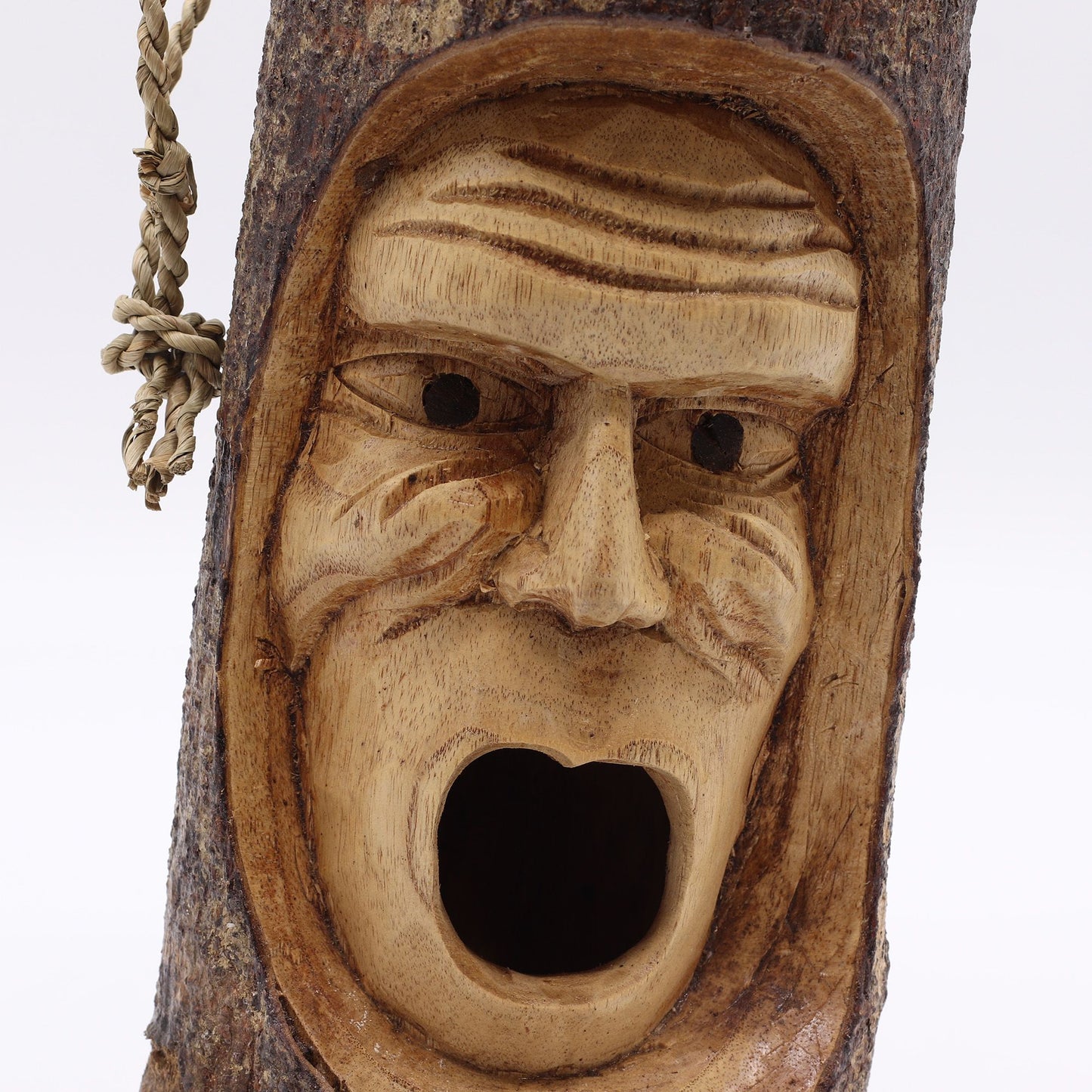 Máscara tallada en madera natural, de color marrón claro, estilo rústico y expresión facial sorprendente.