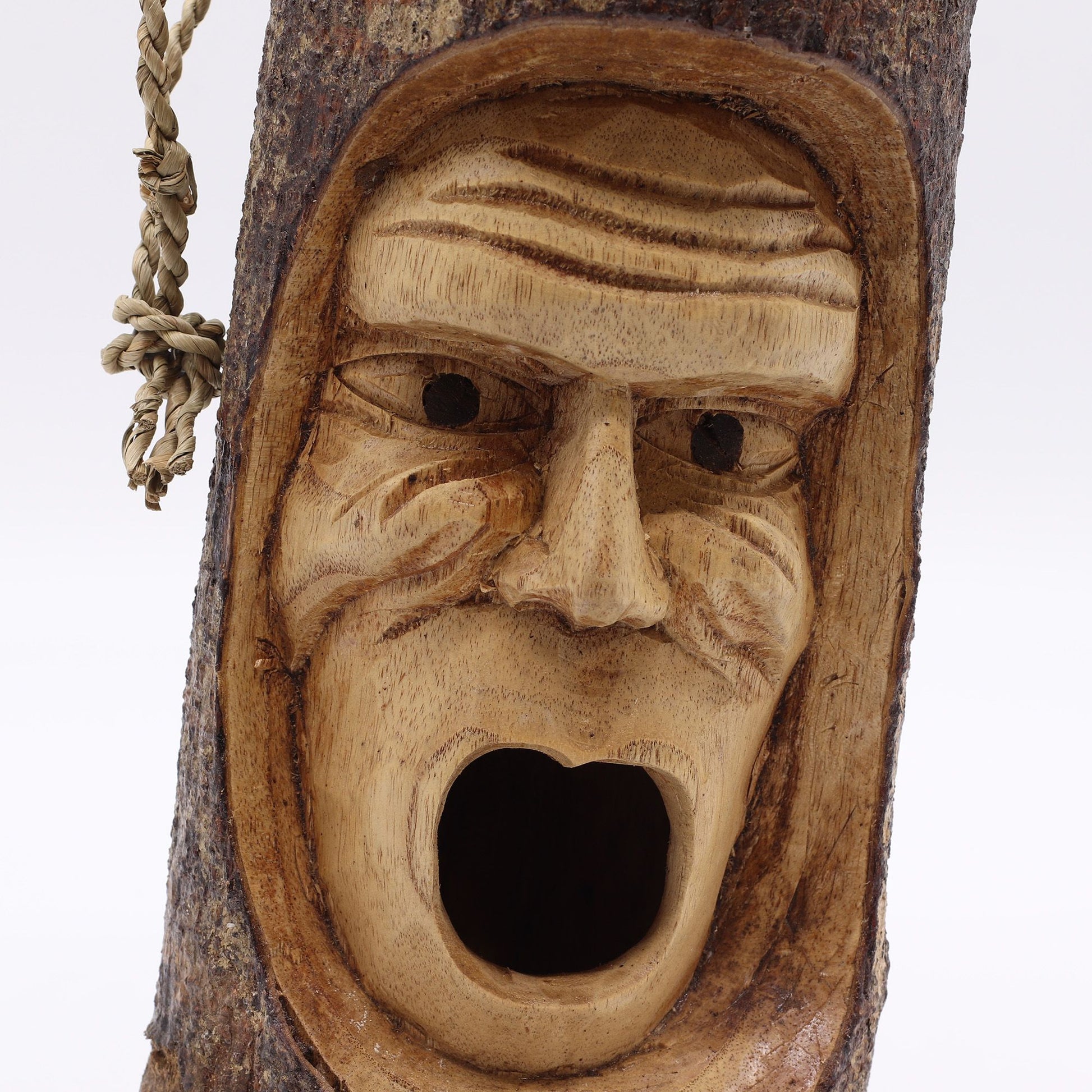 Máscara tallada en madera natural, de color marrón claro, estilo rústico y expresión facial sorprendente.