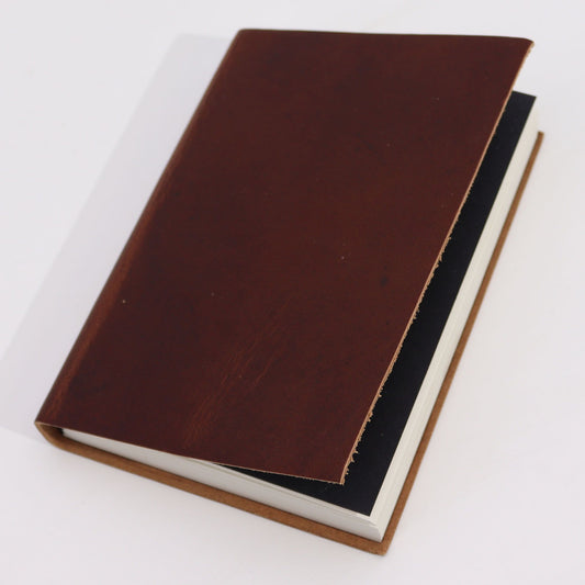 Cuaderno de estilo rústico con cubierta de cuero marrón oscuro y hojas blancas sobre fondo blanco neutro