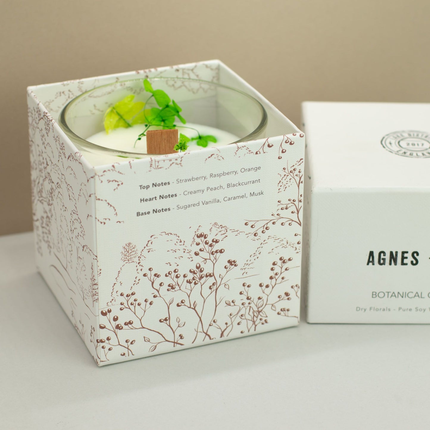 Vela aromática de soja con notas de fresa, frambuesa y naranja, en envase blanco y diseño floral elegante.