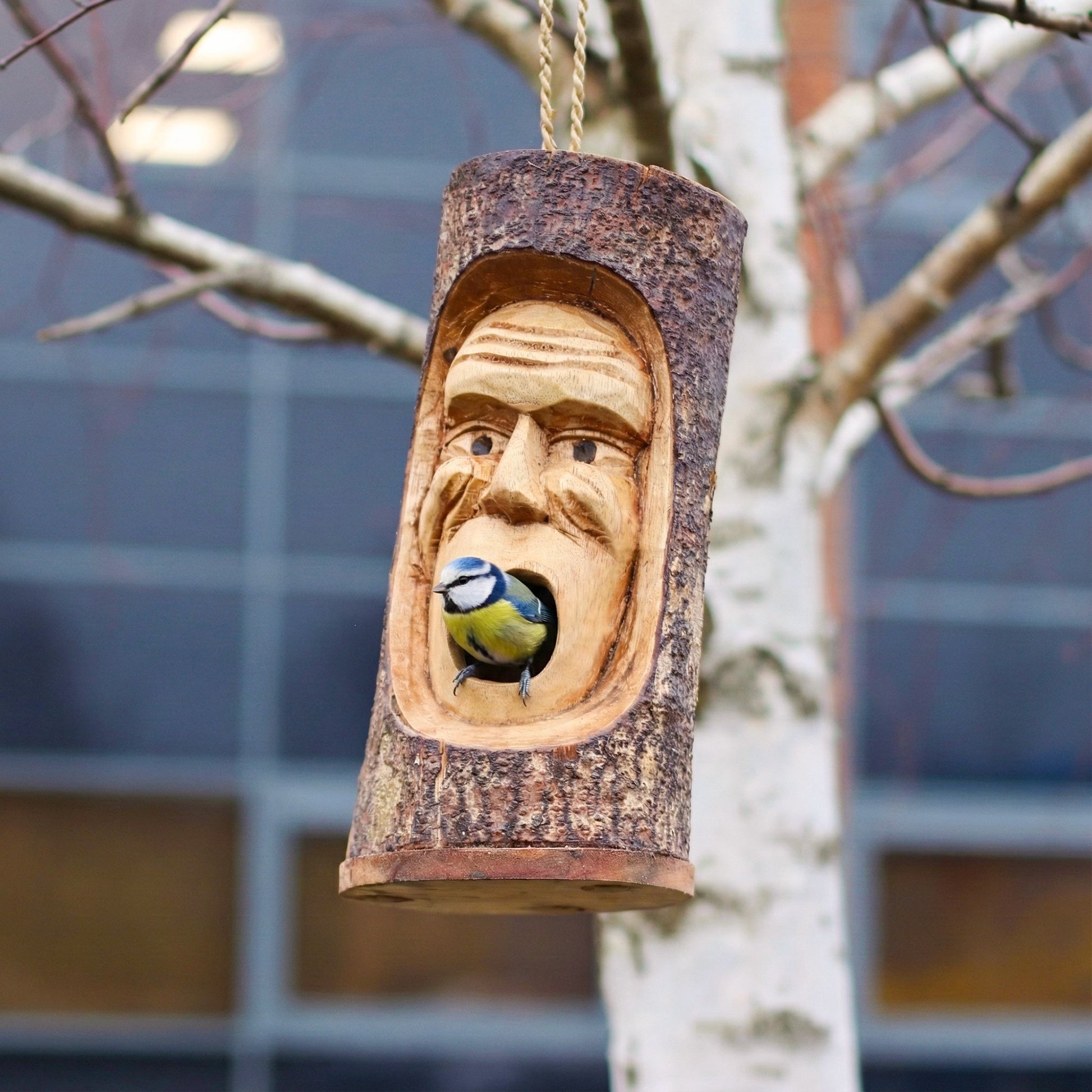 Comedero de pájaros de madera tallada en forma de cara, con color natural y diseño rústico, ideal para exteriores.