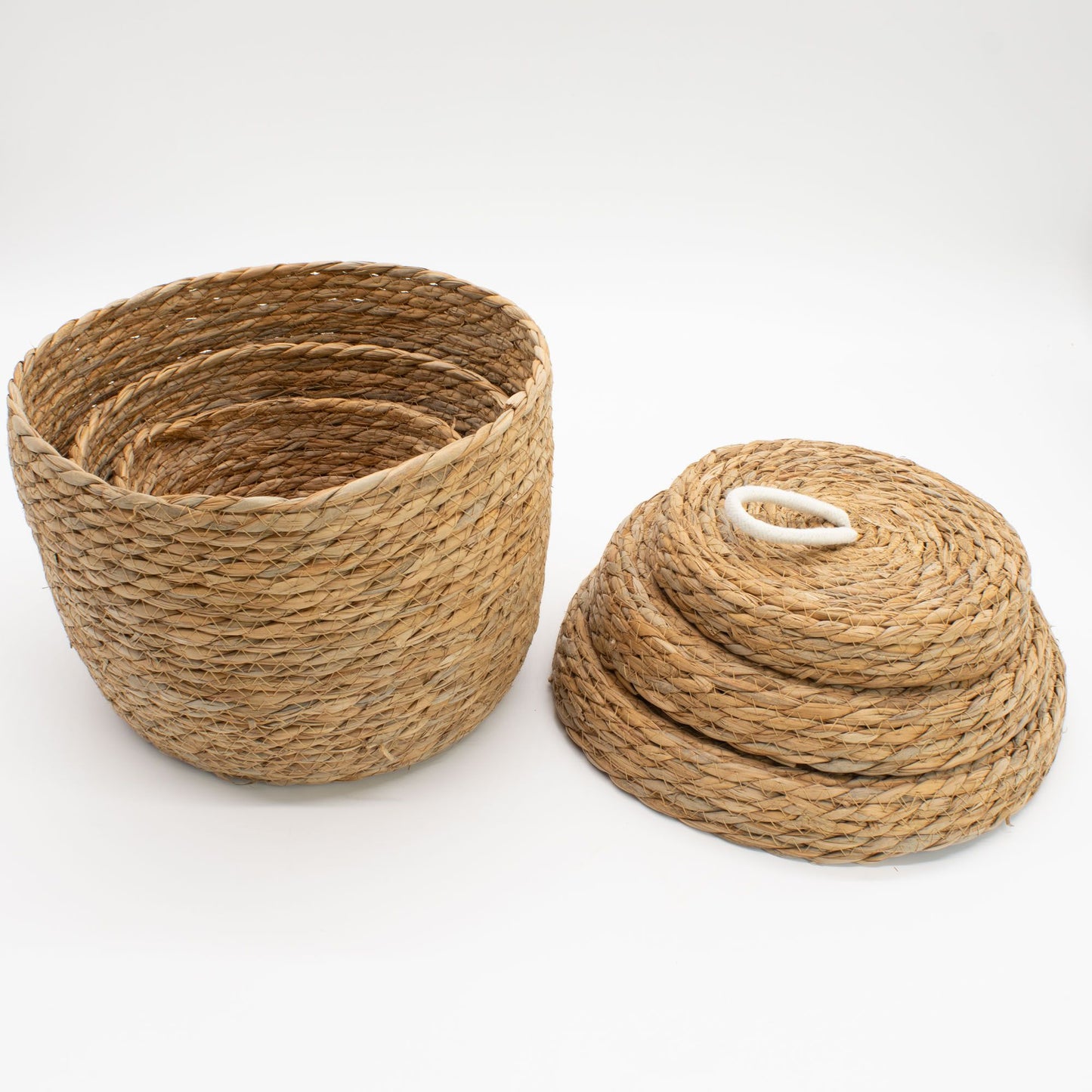 Juego de 3 cestas redondas de hierba marina trenzada natural, apiladas con tapas y detalle de asa de algodón blanco.