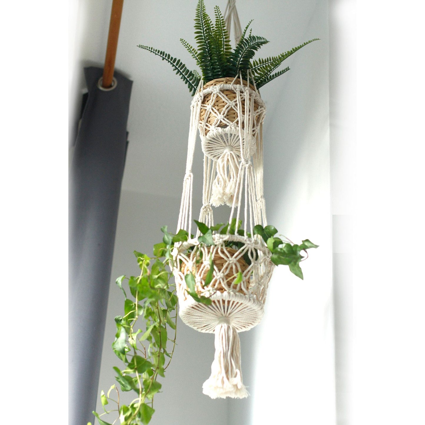 Macramé colgante en color crema con dos macetas de plantas verdes en un estilo bohemio.