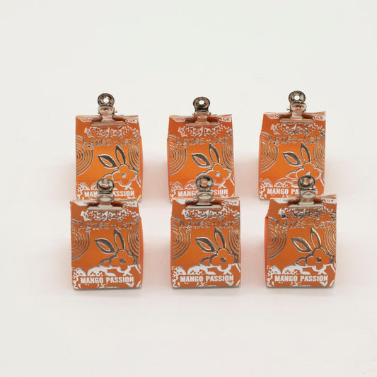 Seis bálsamos labiales naranja de Agnes + Cat con diseño floral plateado y pinza metálica superior sobre fondo blanco.