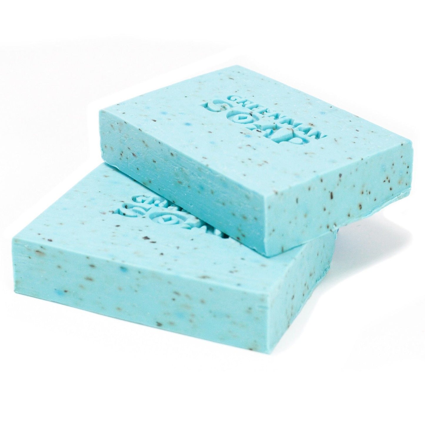 Dos pastillas de jabón azul claro, con motas oscuras y grabado "Greenman Soap" sobre fondo blanco.
