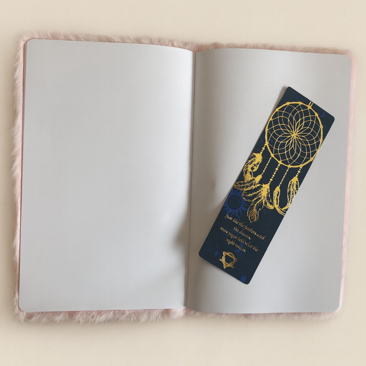 Marcador de sueños azul marino con diseño dorado en un cuaderno rosa suave. Ideal para amantes de la lectura.