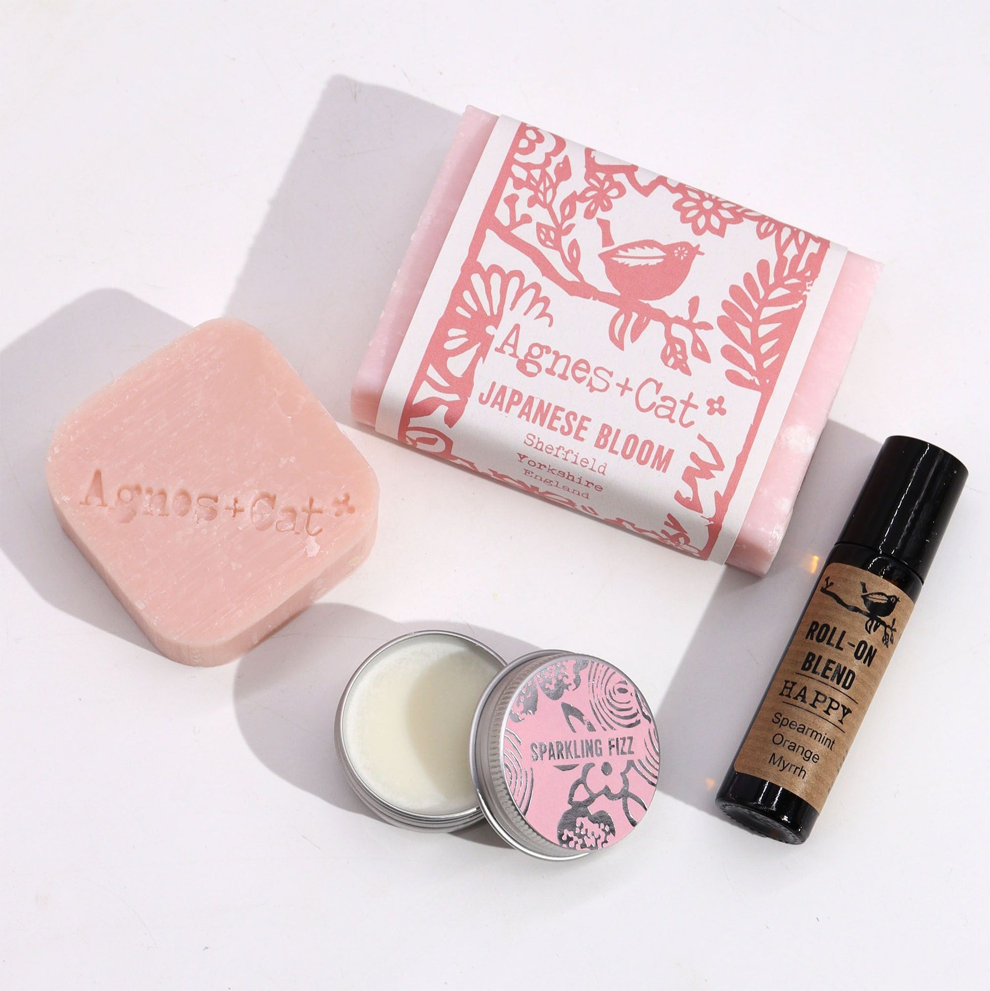 Set de regalo Agnes & Cat: jabón rosa, bálsamo en lata "Sparkling Fizz" y aceite esencial roll-on en frasco oscuro.