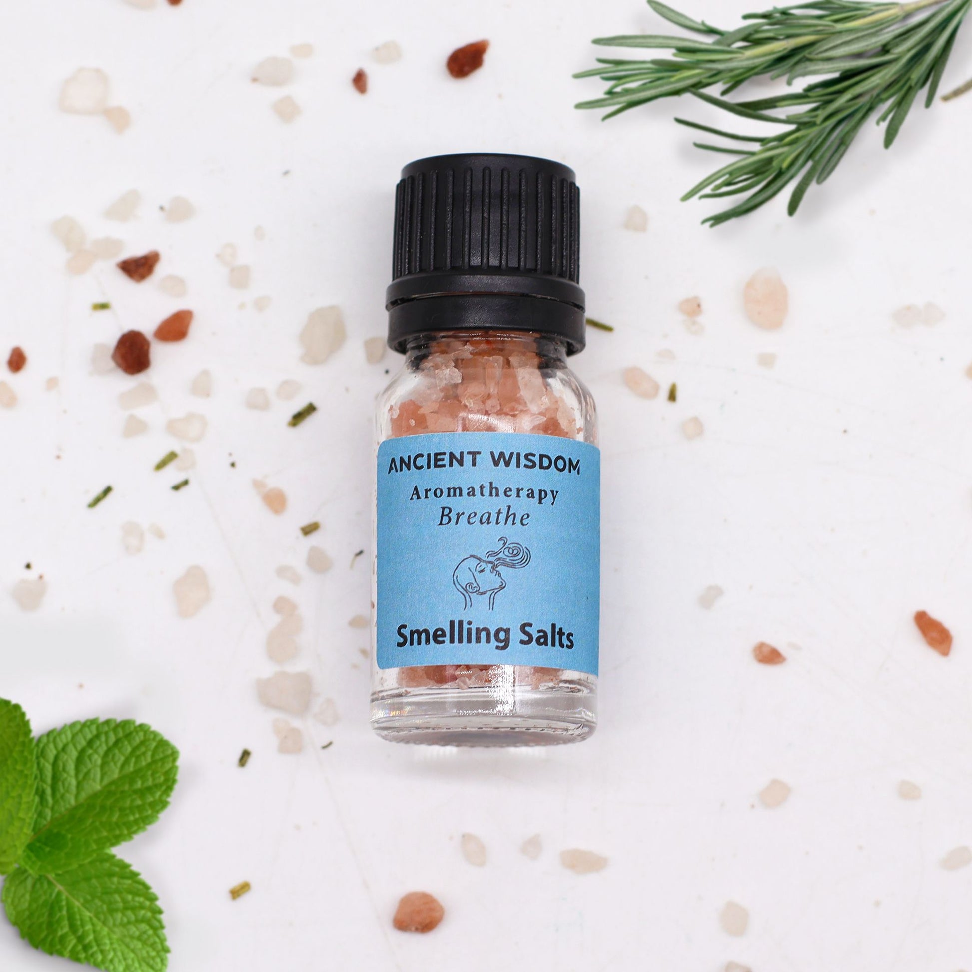 Frasco de sales aromáticas Ancient Wisdom, etiqueta azul, rodeado de sal gruesa, una rama de romero y hojas de menta.