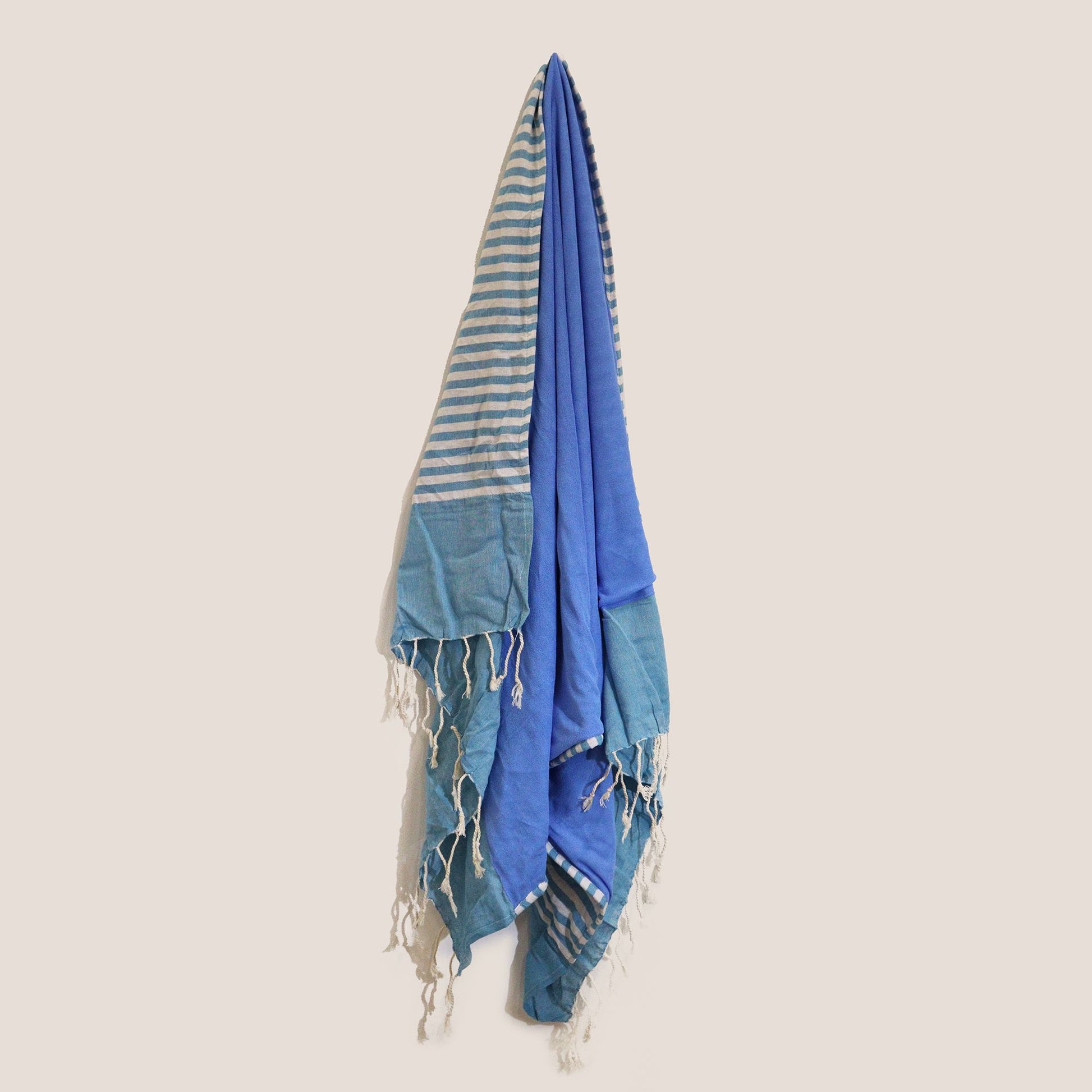 Toalla de playa de algodón azul y gris con franjas y flecos, ideal para verano y días de piscina.