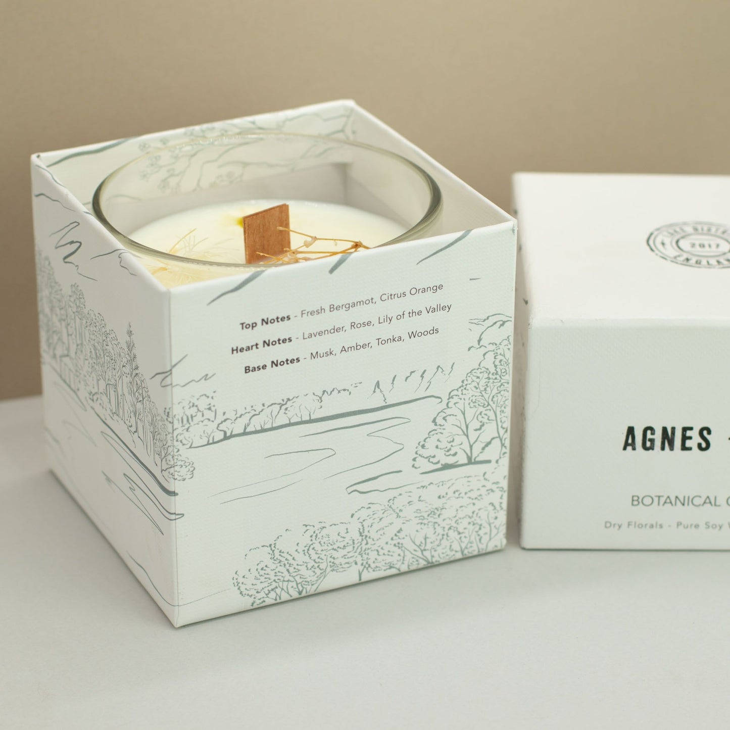 Vela de soya blanca con fragancias florales, en caja blanca decorada con ilustraciones naturales.
