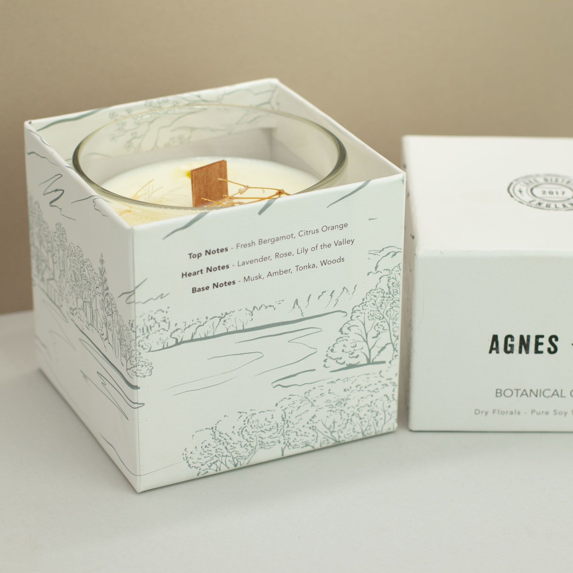 Vela de soya blanca con fragancias florales, en caja blanca decorada con ilustraciones naturales.