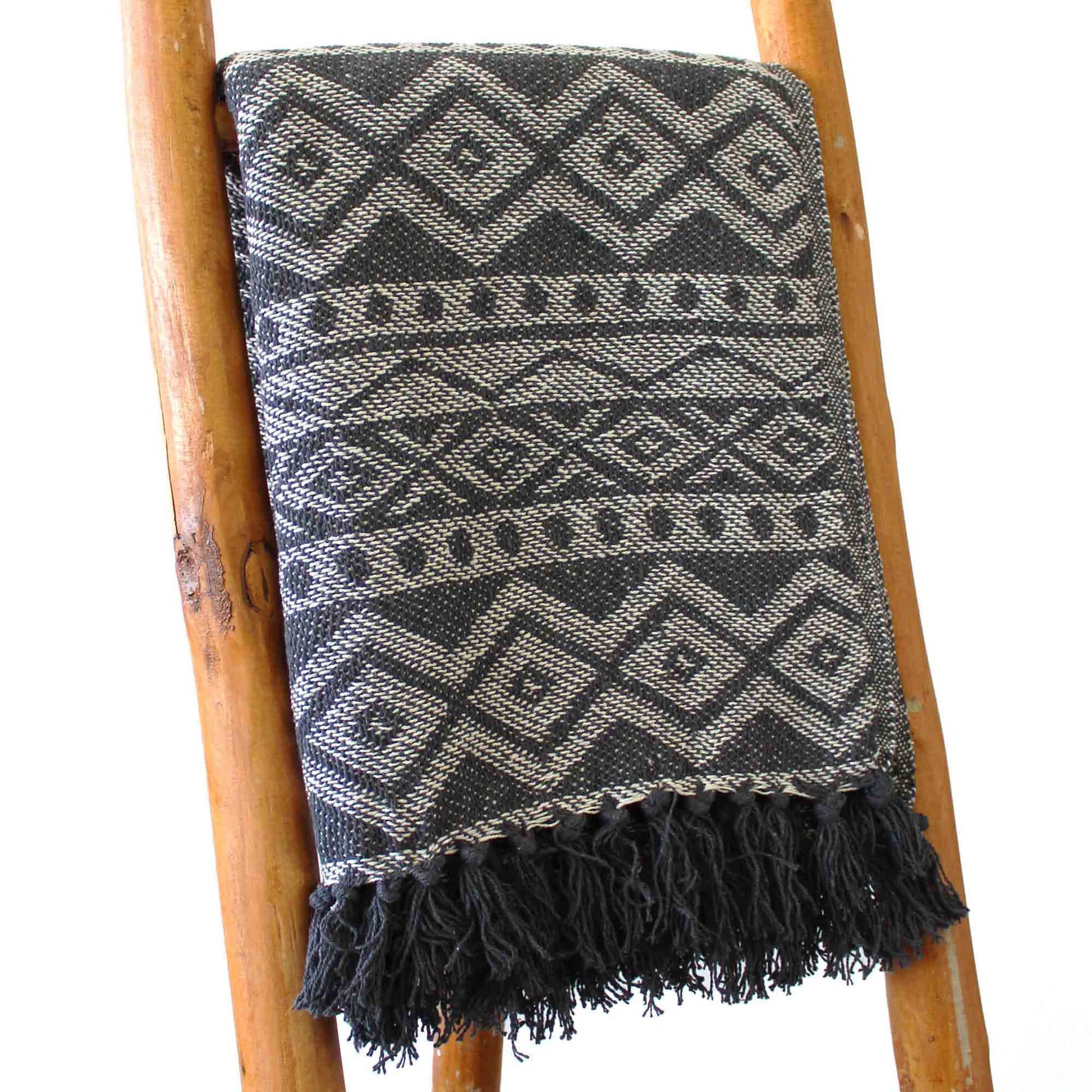 Manta tejida en negro y gris con diseño de diamantes y flecos, ideal para decoración bohemia.