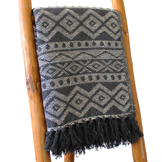 Manta tejida en negro y gris con diseño de diamantes y flecos, ideal para decoración bohemia.