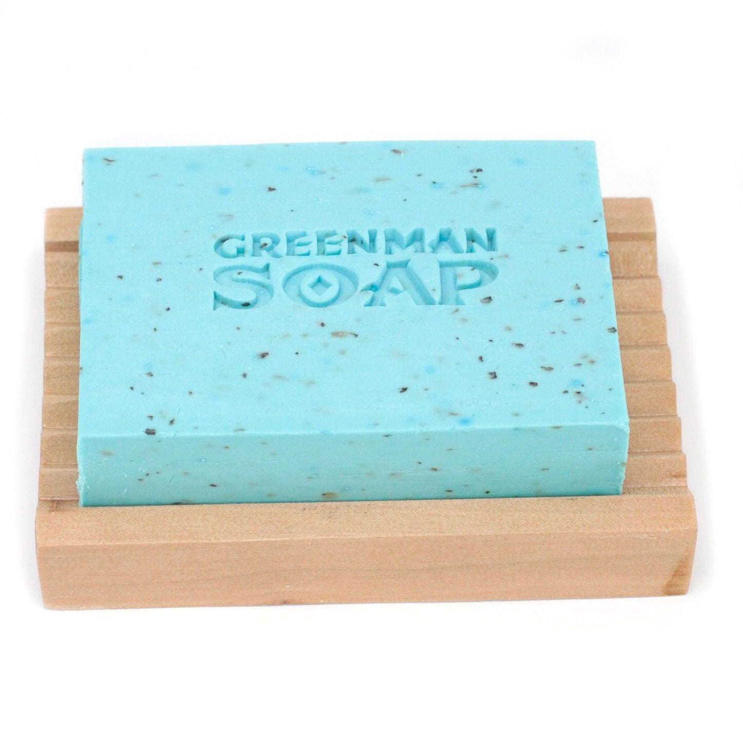 Jabón rectangular azul claro, con motas oscuras y grabado "GREENMAN SOAP", sobre una jabonera de madera acanalada.