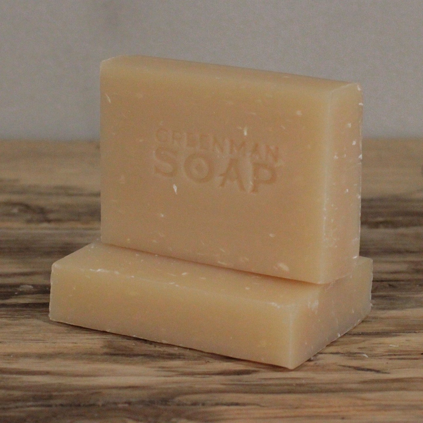 Dos pastillas de jabón beige artesanal, una sobre otra, con la marca "Greenman Soap" grabada en la superficie.