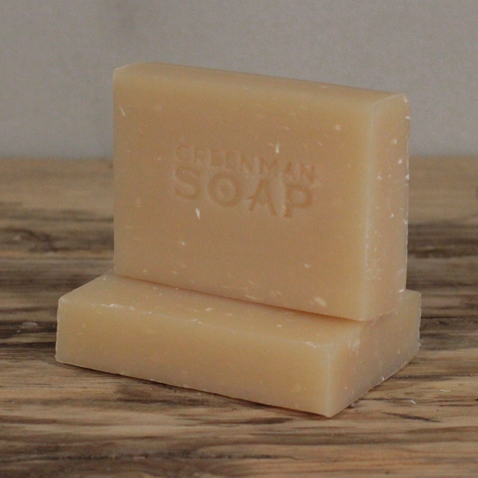 Dos pastillas de jabón beige artesanal, una sobre otra, con la marca "Greenman Soap" grabada en la superficie.
