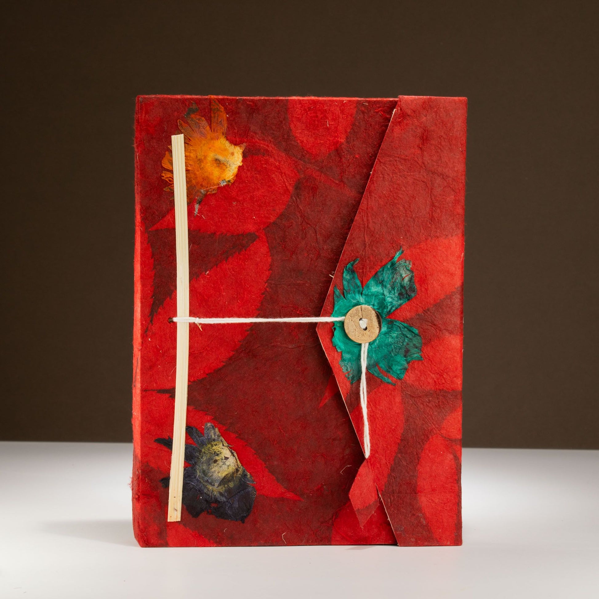 Cuaderno artesanal de papel reciclado rojo con flores secas, cierre de cuerda y botón. Ideal para anotaciones.