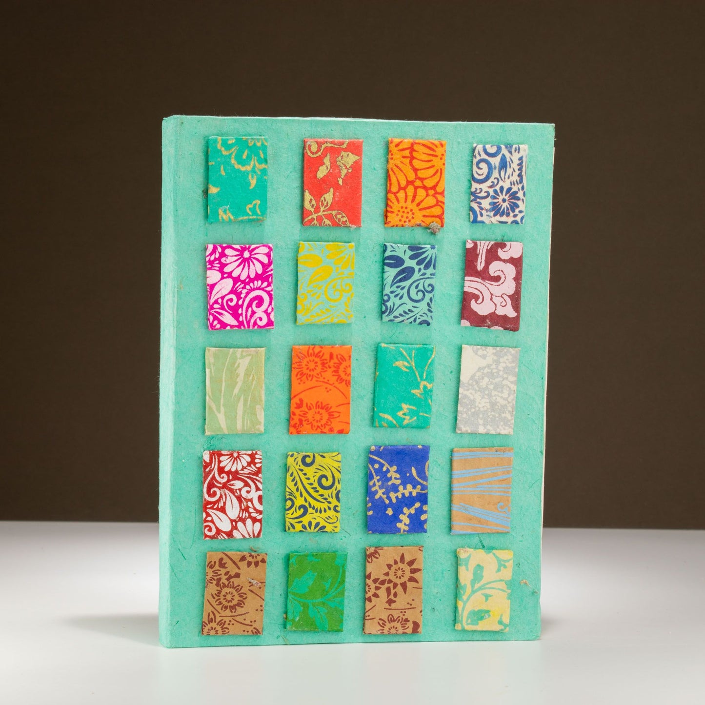 Cuaderno de papel reciclado en color aqua con estampados coloridos en la portada, estilo artesanal y vibrante.