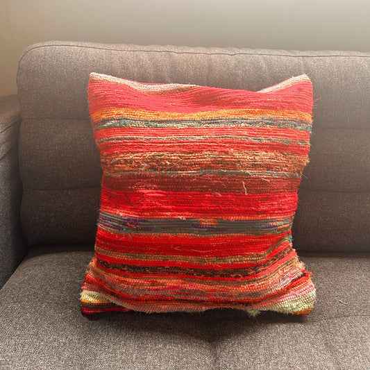 Funda de cojín artesanal de 40x40cm con diseño de rayas tejidas en tonos rojos y textura rústica sobre un sofá gris