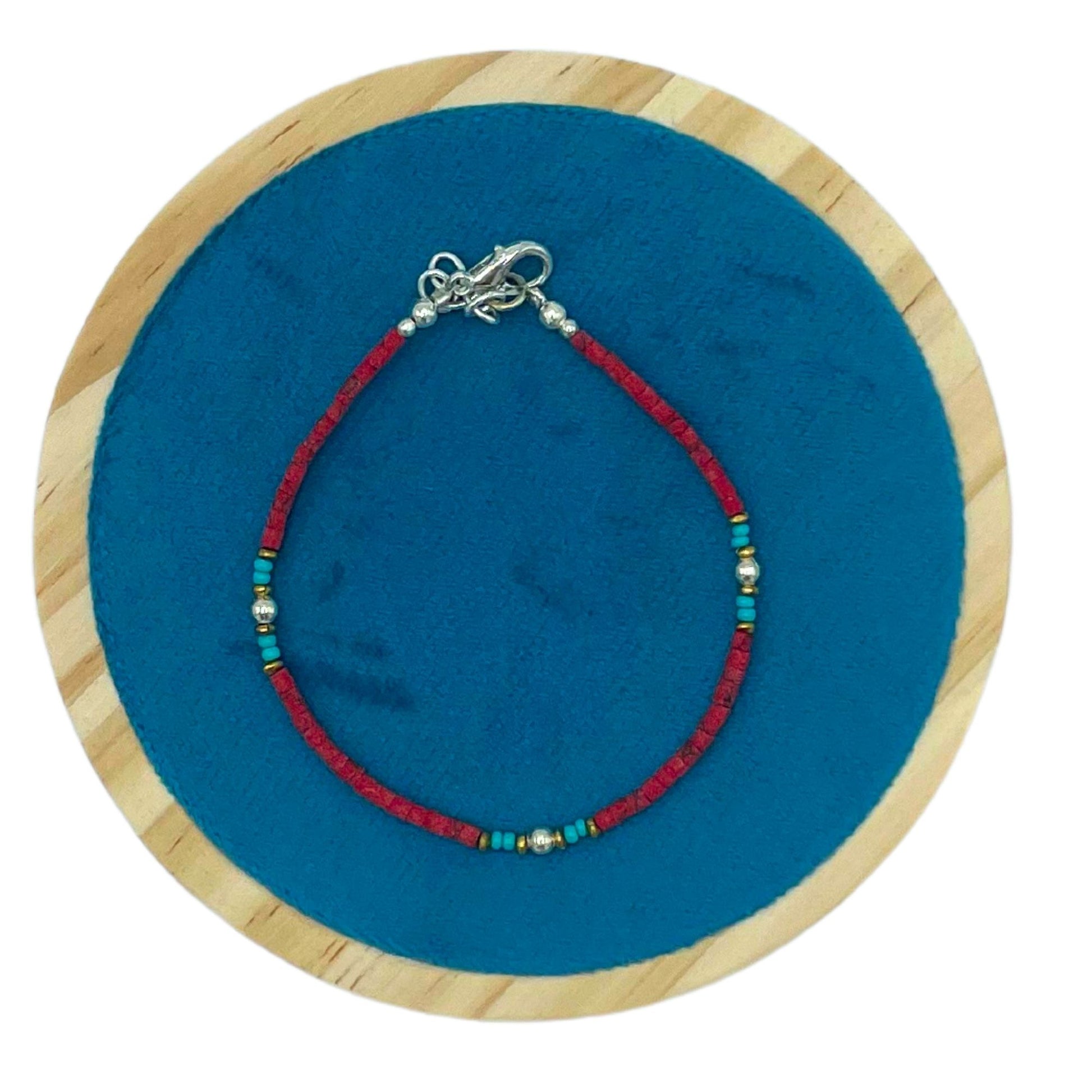 Pulsera artesanal de cuentas rojas y verdes con cierre de plata, sobre fondo azul, estilo bohemio.
