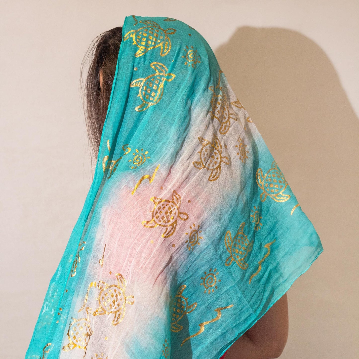 Bufanda de gasa azul turquesa con estampado dorado de tortugas y diseño degradado. Ideal para un look veraniego.