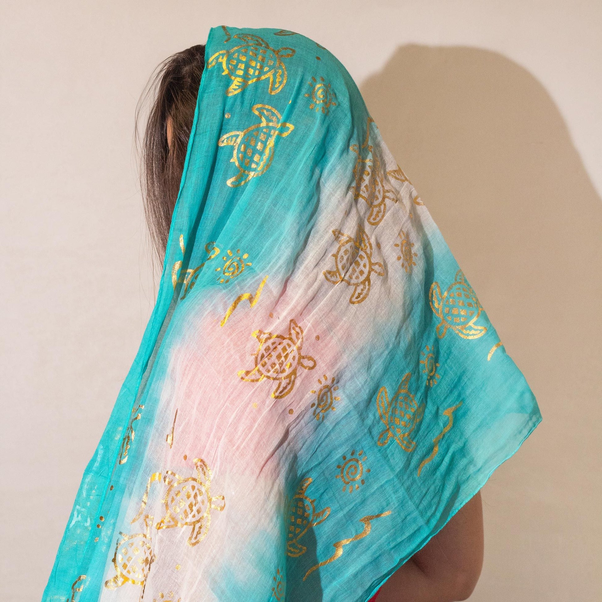 Bufanda de gasa azul turquesa con estampado dorado de tortugas y diseño degradado. Ideal para un look veraniego.