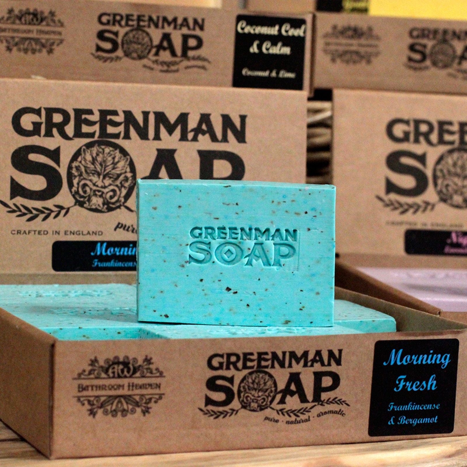 Jabón artesanal turquesa con texturas, marca "Greenman Soap" grabado, en caja de cartón kraft con etiquetas informativas.