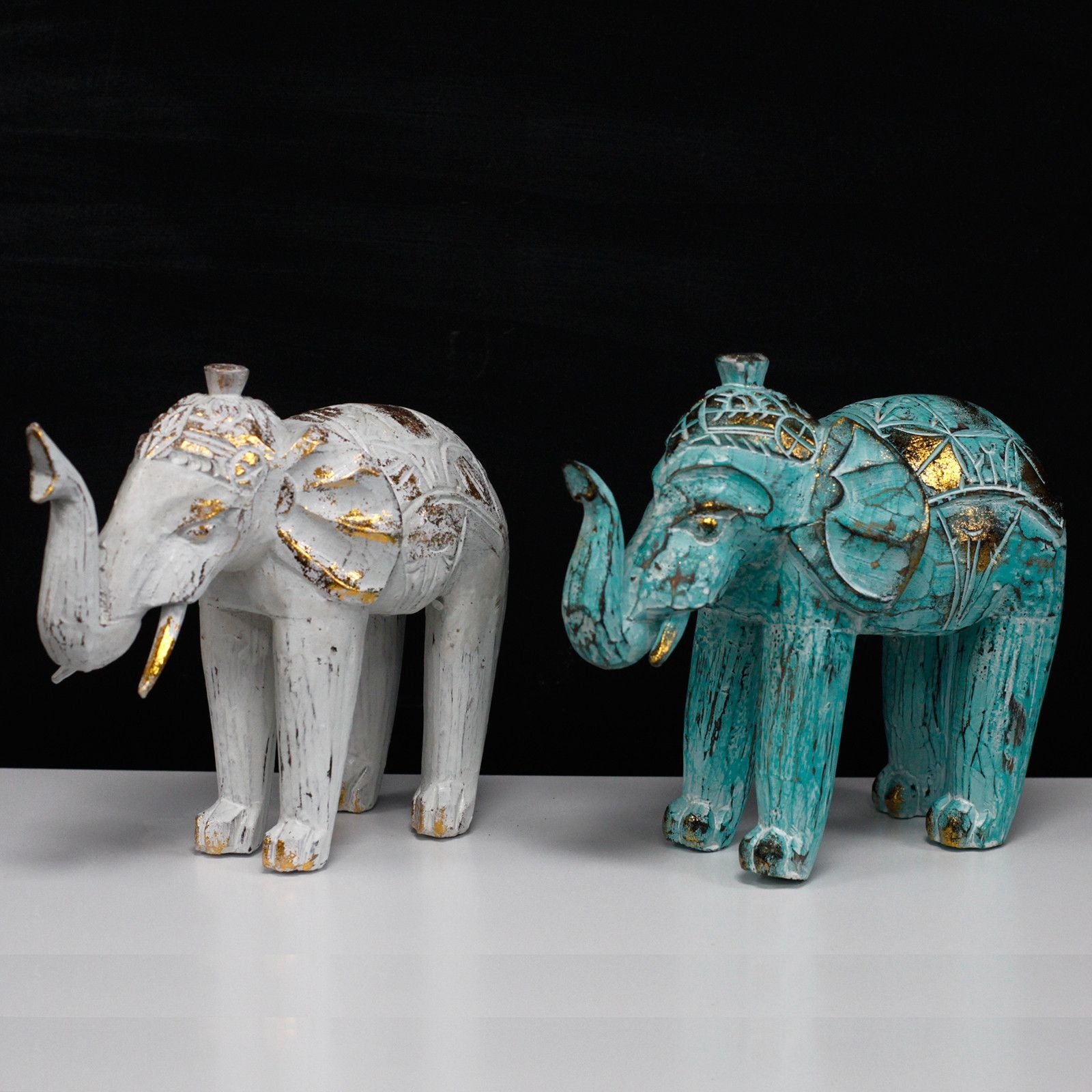 Elefantes decorativos de madera, uno blanco con dorado y otro azul turquesa, estilo bohemio y artesanal.