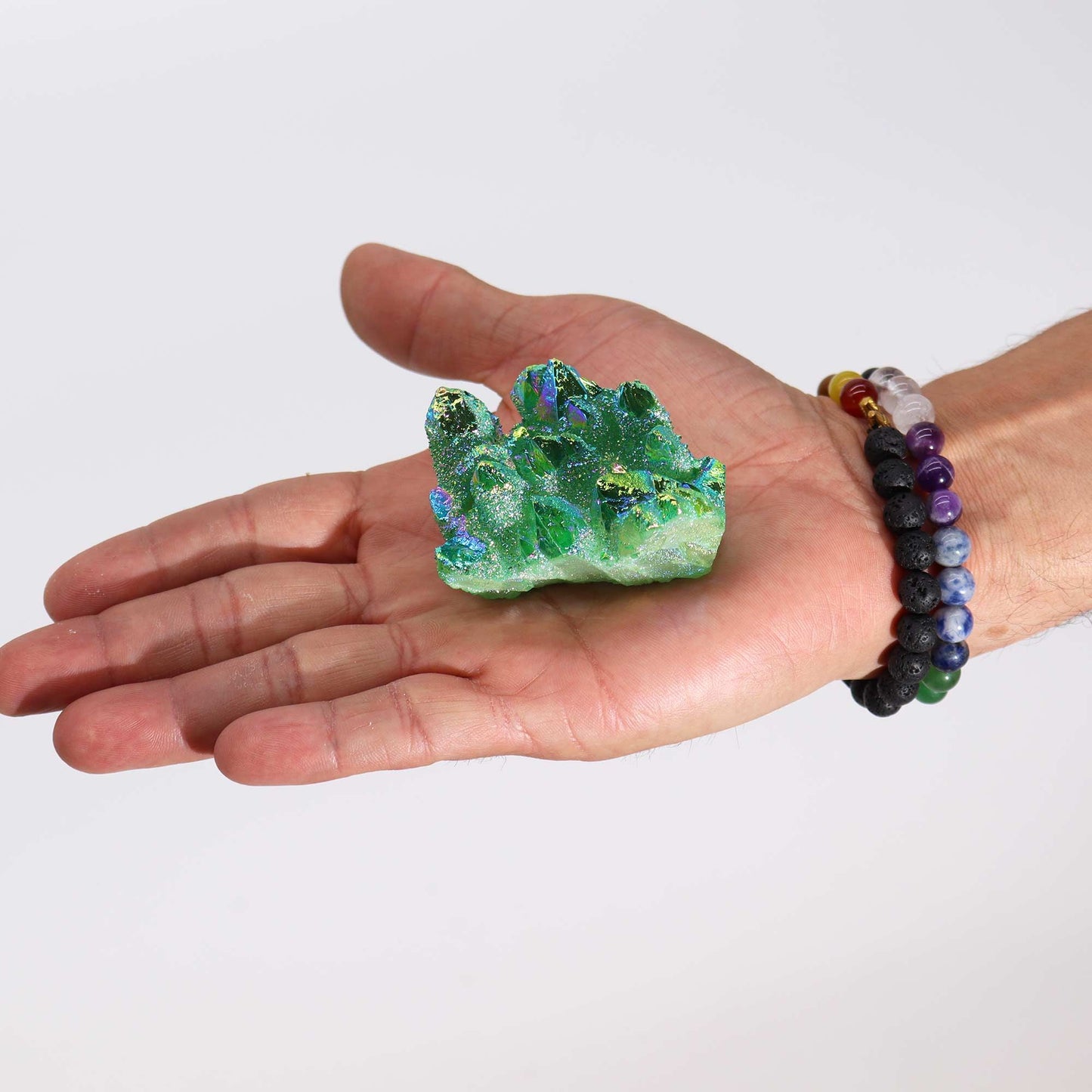 Cristal verde brillante con destellos, sobre mano masculina, adornado con pulseras de piedras naturales.