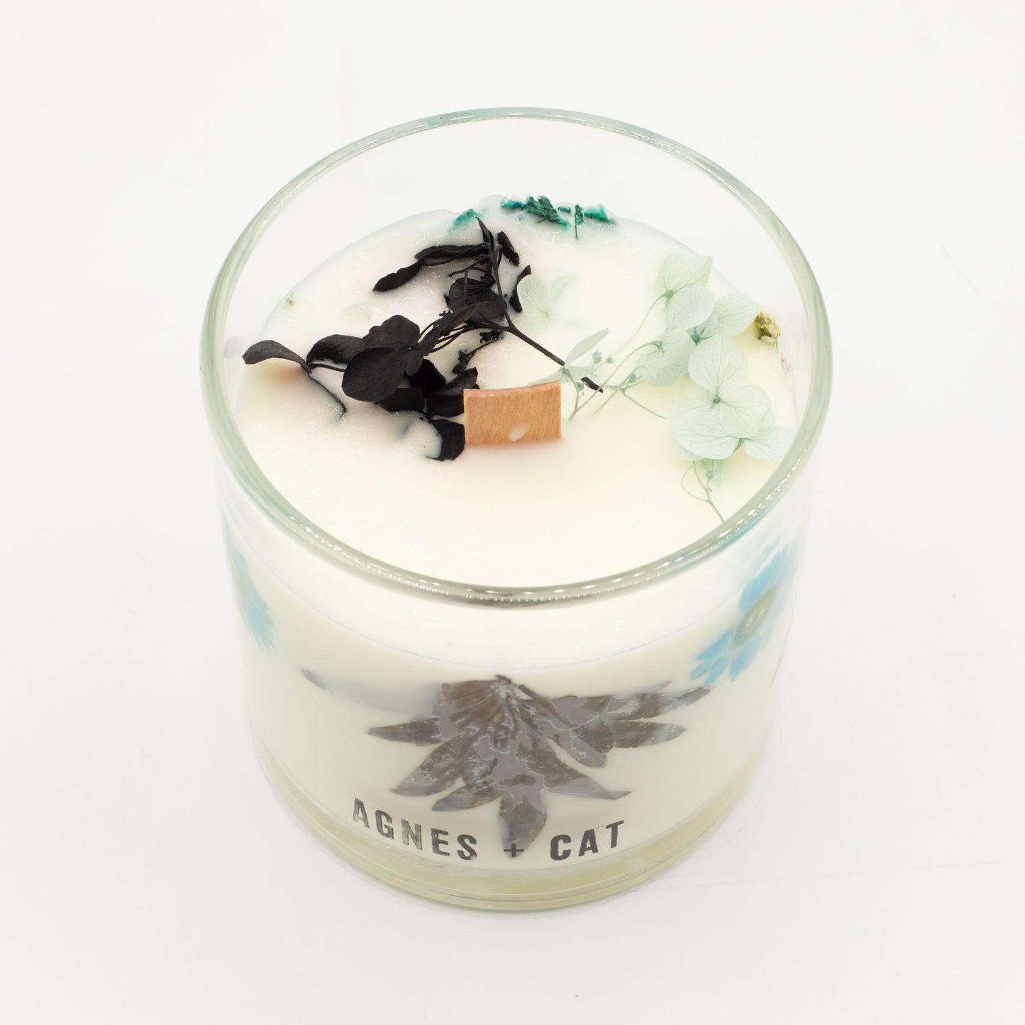 Vela aromática blanca con flores secas, detalles en azul y tapa de madera, estilo elegante y natural.