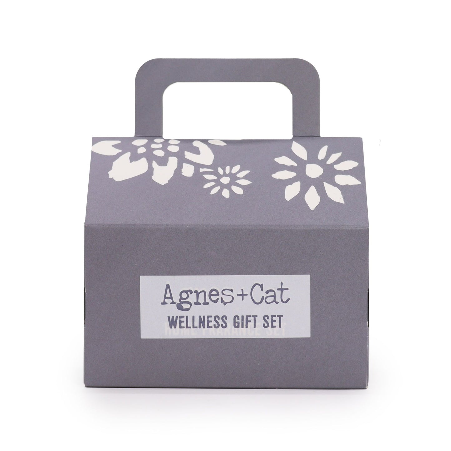 Caja de regalo gris con asa, detalles florales blancos y etiqueta central "Agnes + Cat Wellness Gift Set".