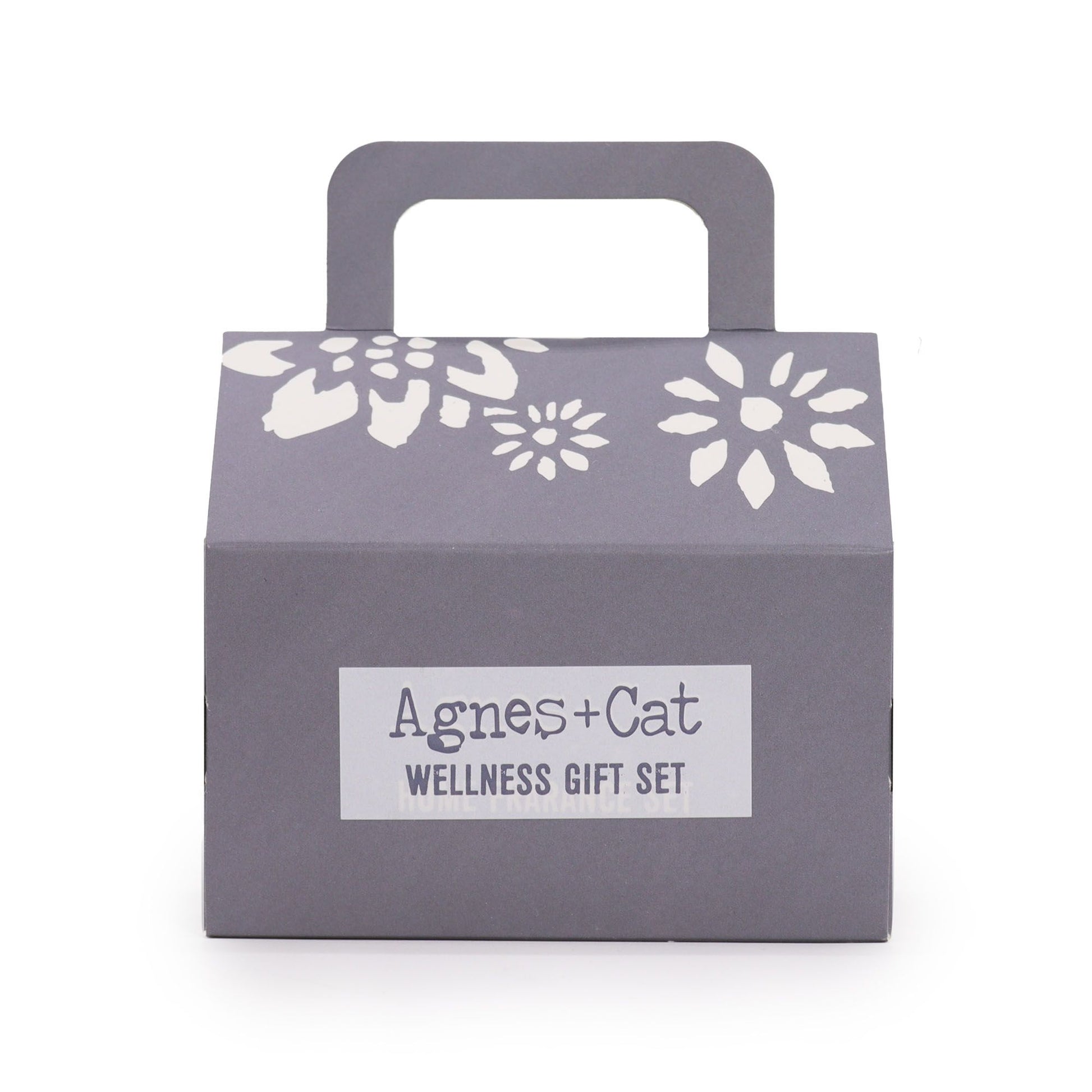 Caja de regalo gris con asa, detalles florales blancos y etiqueta central "Agnes + Cat Wellness Gift Set".