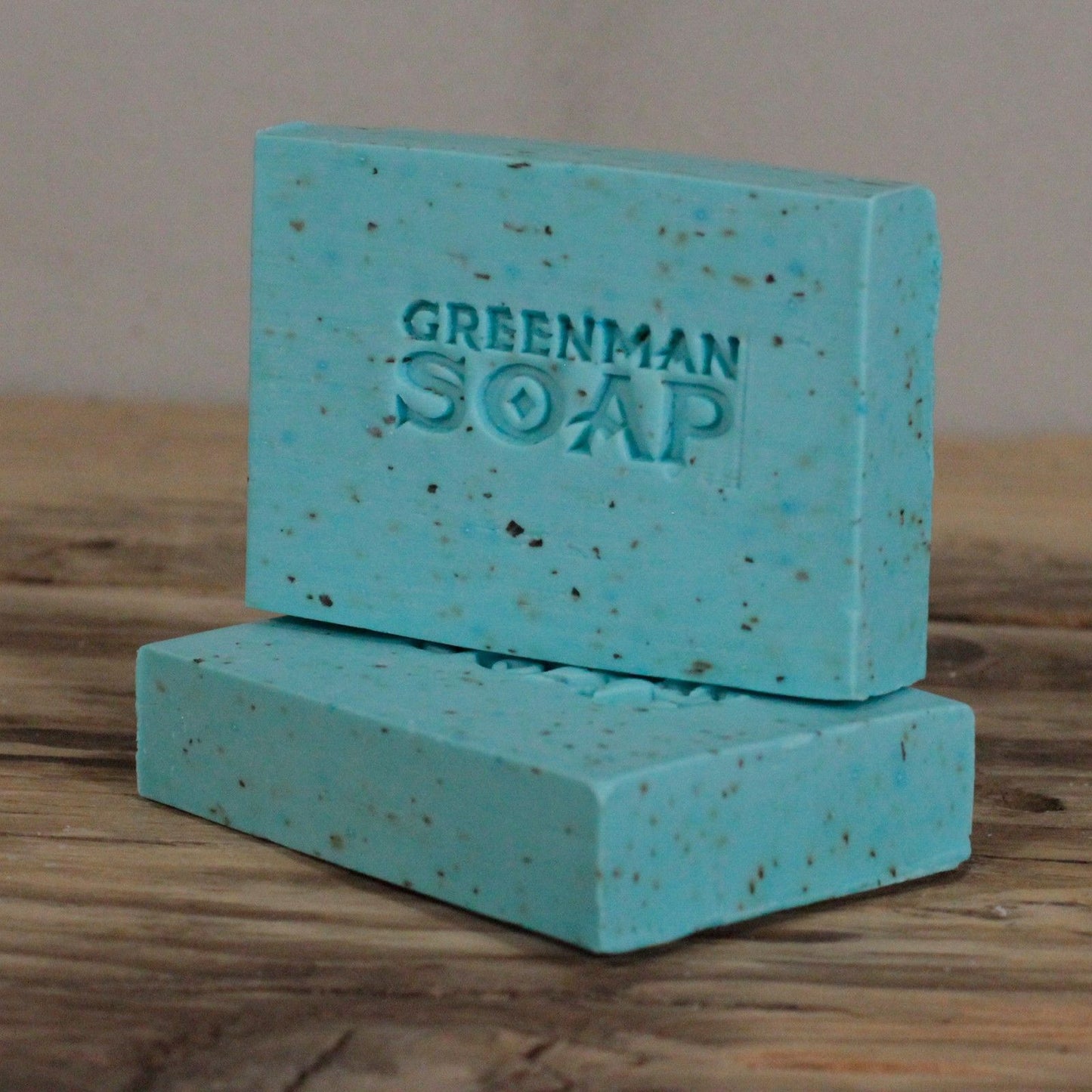 Dos pastillas de jabón azul claro con motas, marcadas con "GREENMAN SOAP", sobre una superficie de madera rústica.