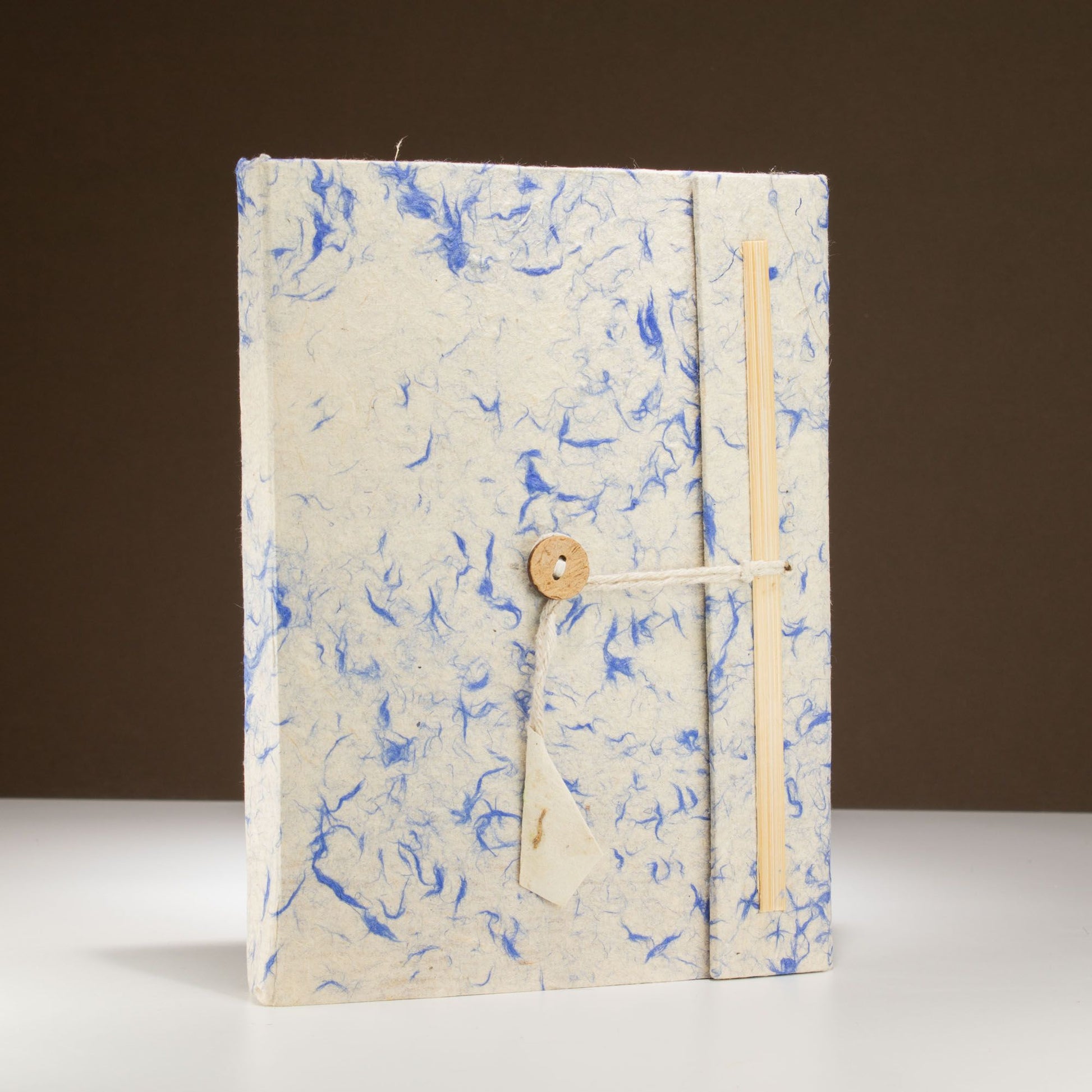Cuaderno artesanal en papel reciclado azul y blanco, con cierre de cuerda y botón de madera.
