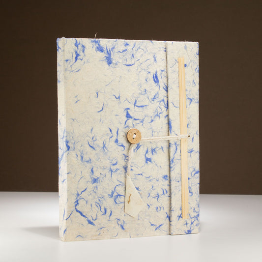 Cuaderno artesanal en papel reciclado azul y blanco, con cierre de cuerda y botón de madera.