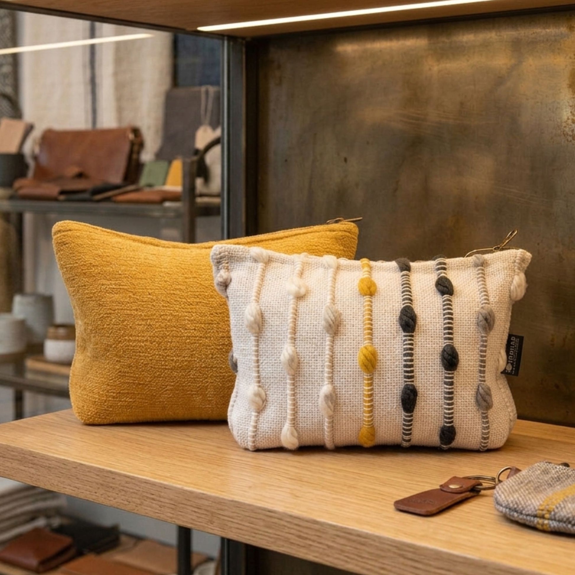 Cojín amarillo y otro blanco con textura, decorado con pompones en gris y amarillo. Ideal para decoración moderna.